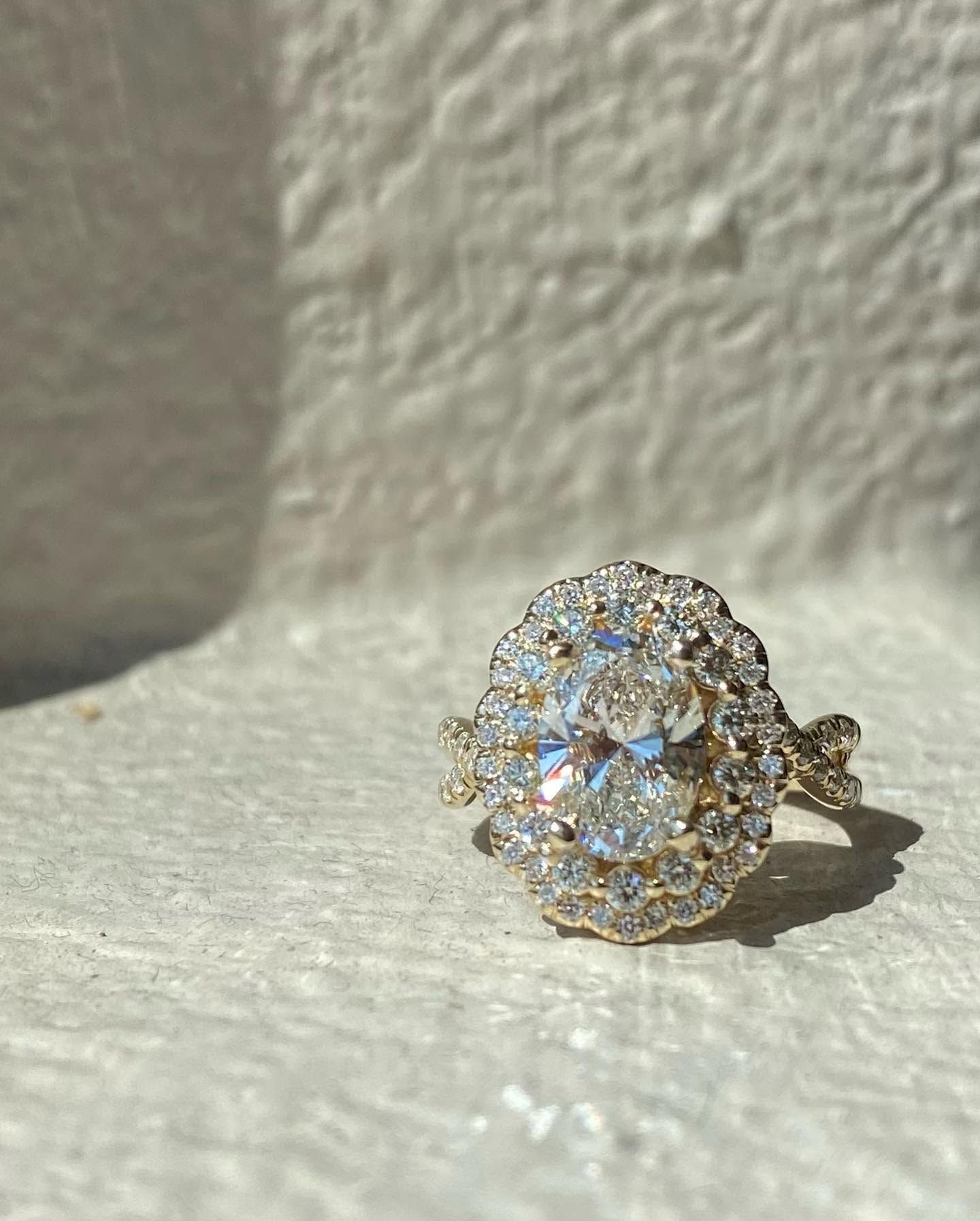 Gold floral halo ring with clear, sparkling stones on a textured beige surface