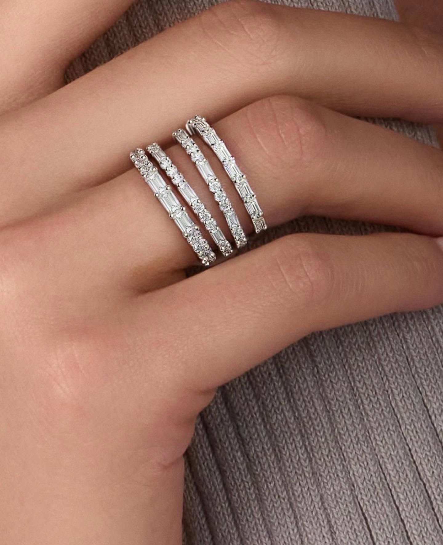 Hand wearing four thin silver and rhinestone rings on a woven beige fabric background
