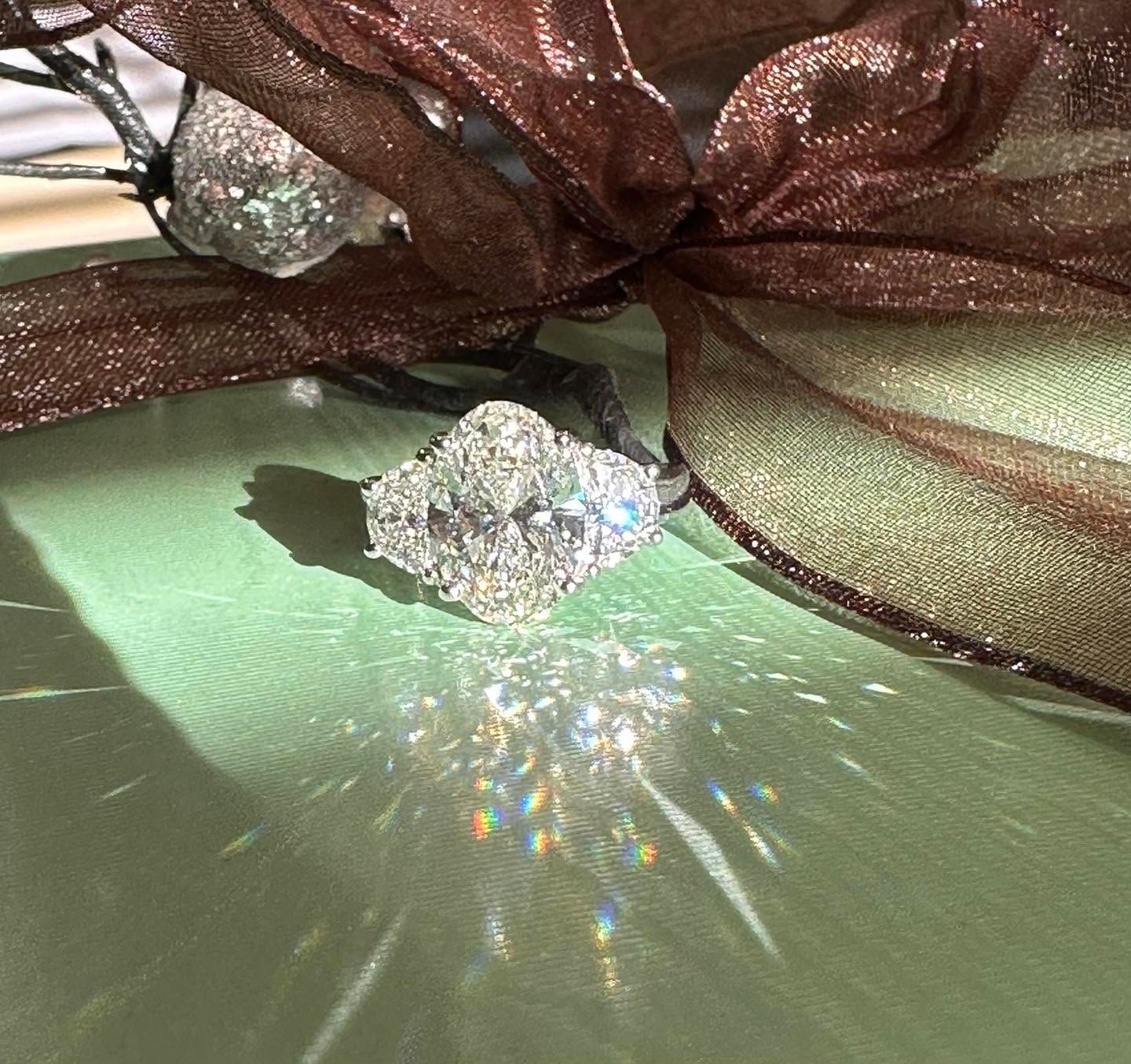 Sparkling silver ring on a pale green surface, with a brown sheer ribbon and prism-like light reflection.