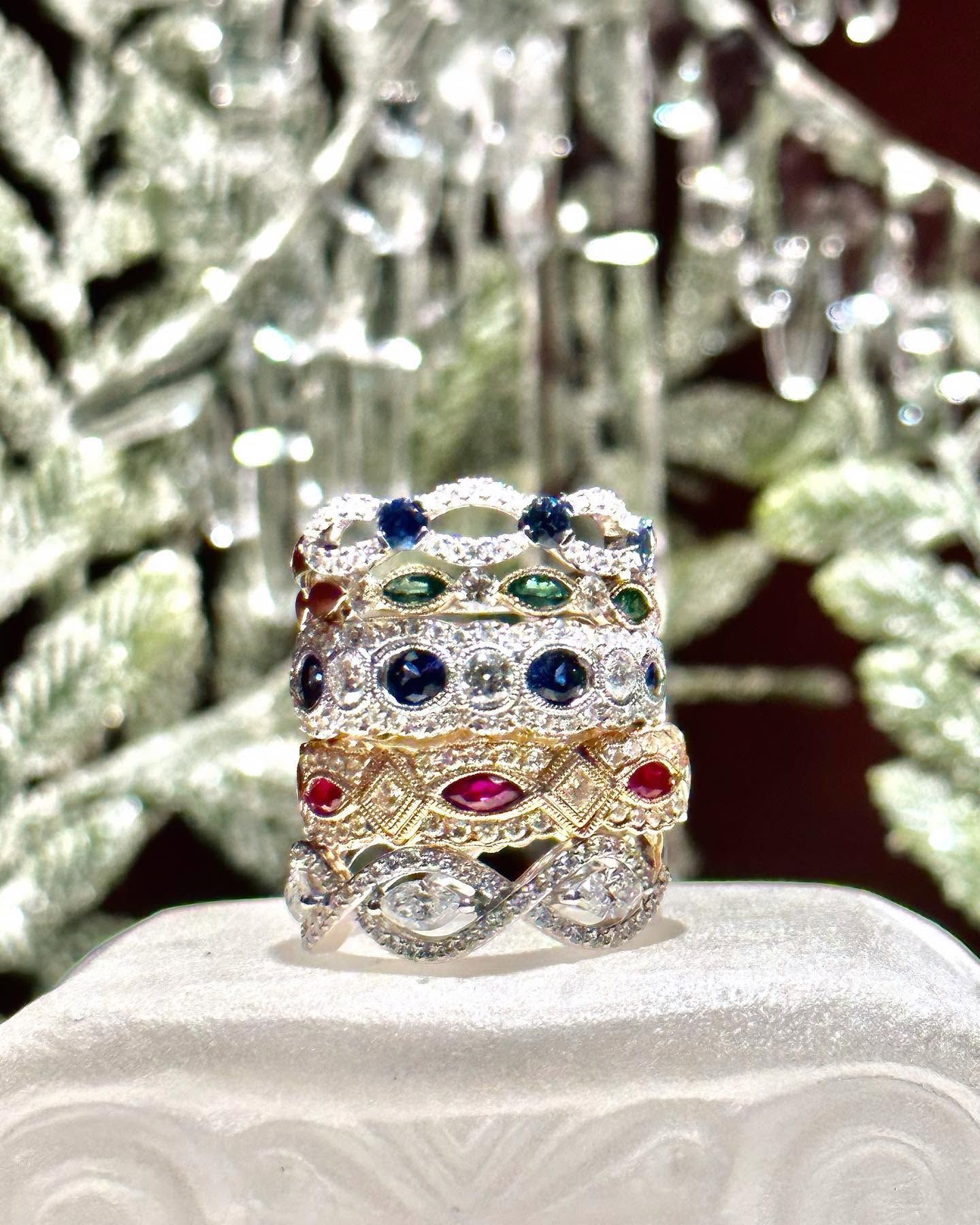 Stacked jeweled rings with blue, green, red, and pink stones on a white display stand
