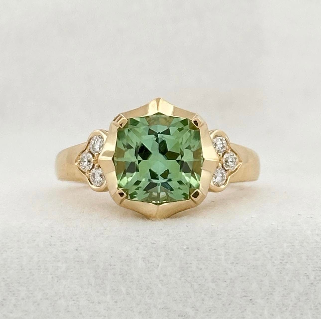 Gold ring with a green cushion-cut gemstone and small clear side stones