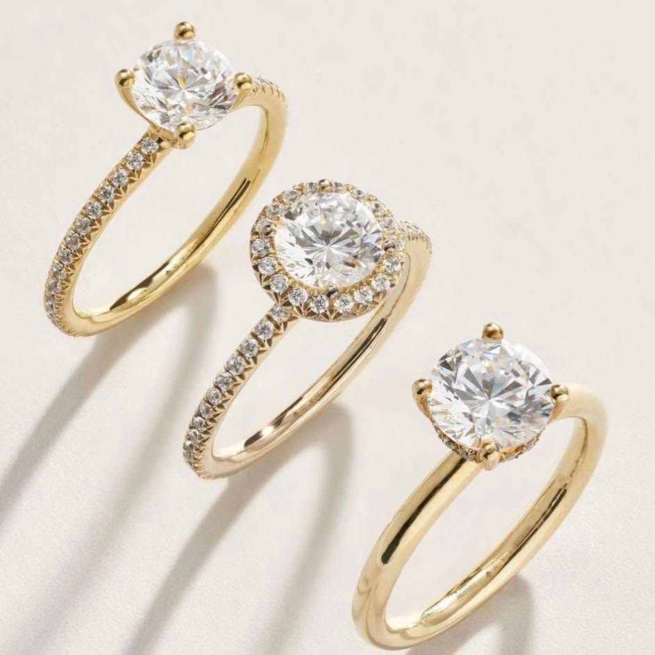 Three gold rings with round clear gemstones on a light background