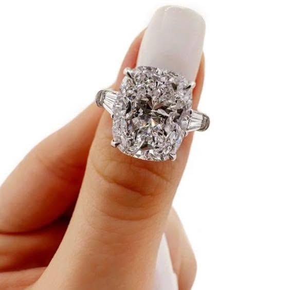 Close-up of a hand wearing a large cushion-cut diamond ring on a white-painted nail