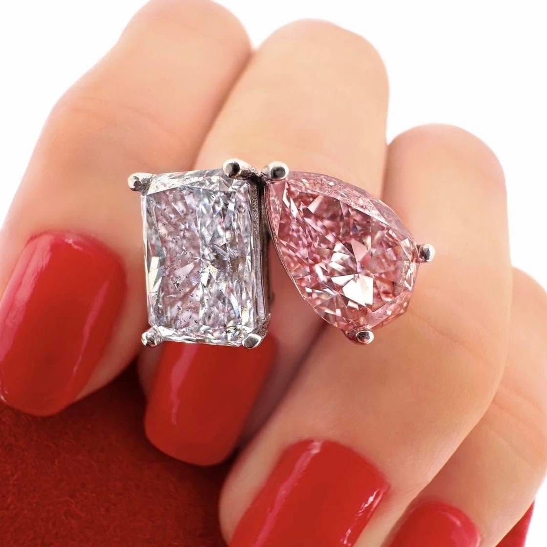 Hand with red nails wearing two gemstone rings, one clear and one pink, on adjacent fingers