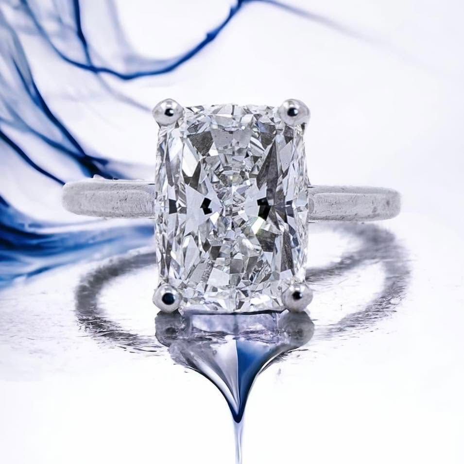 Diamond engagement ring with large rectangular center stone on a white and blue reflective background
