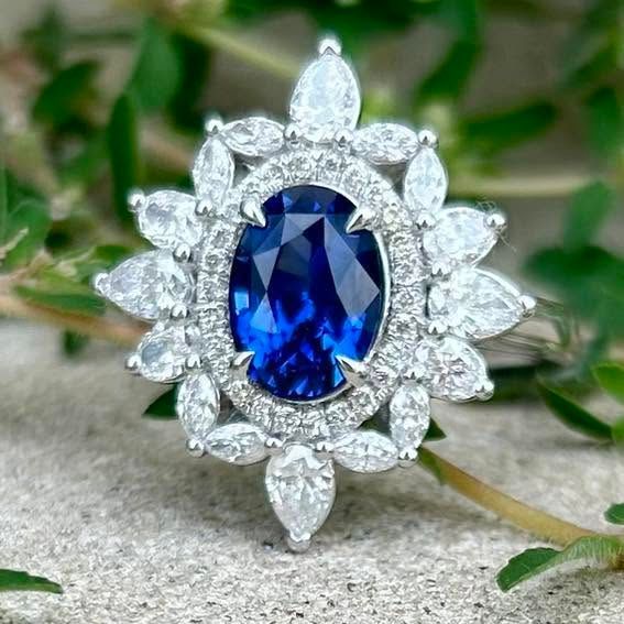 Blue oval gemstone ring with diamond halo on a blurred green background