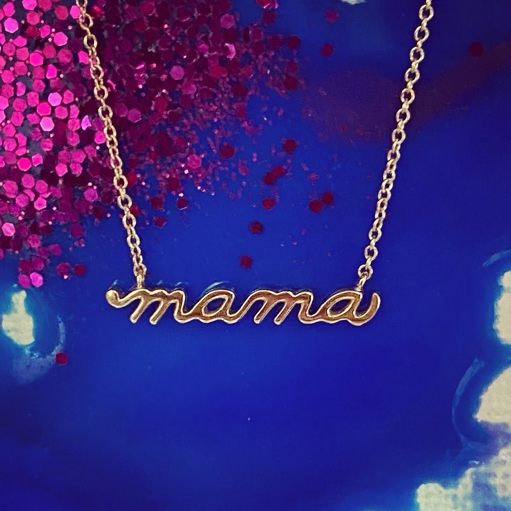 Gold “mama” necklace on a blue background with pink glitter accents