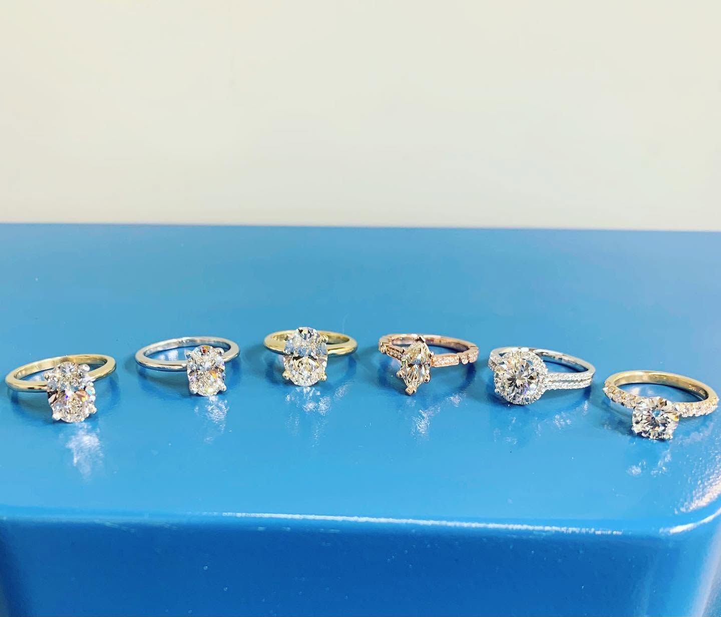 Six diamond rings lined up on a blue surface against a plain background.