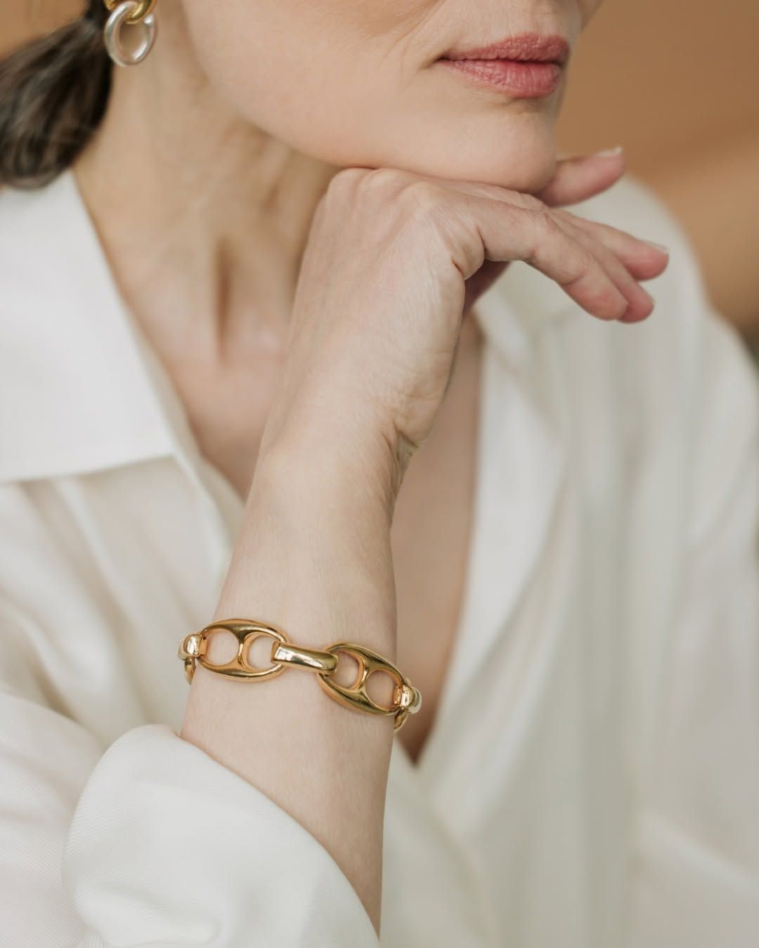 Close-up of a person resting their chin on a hand, wearing a gold chain bracelet and white blouse.
