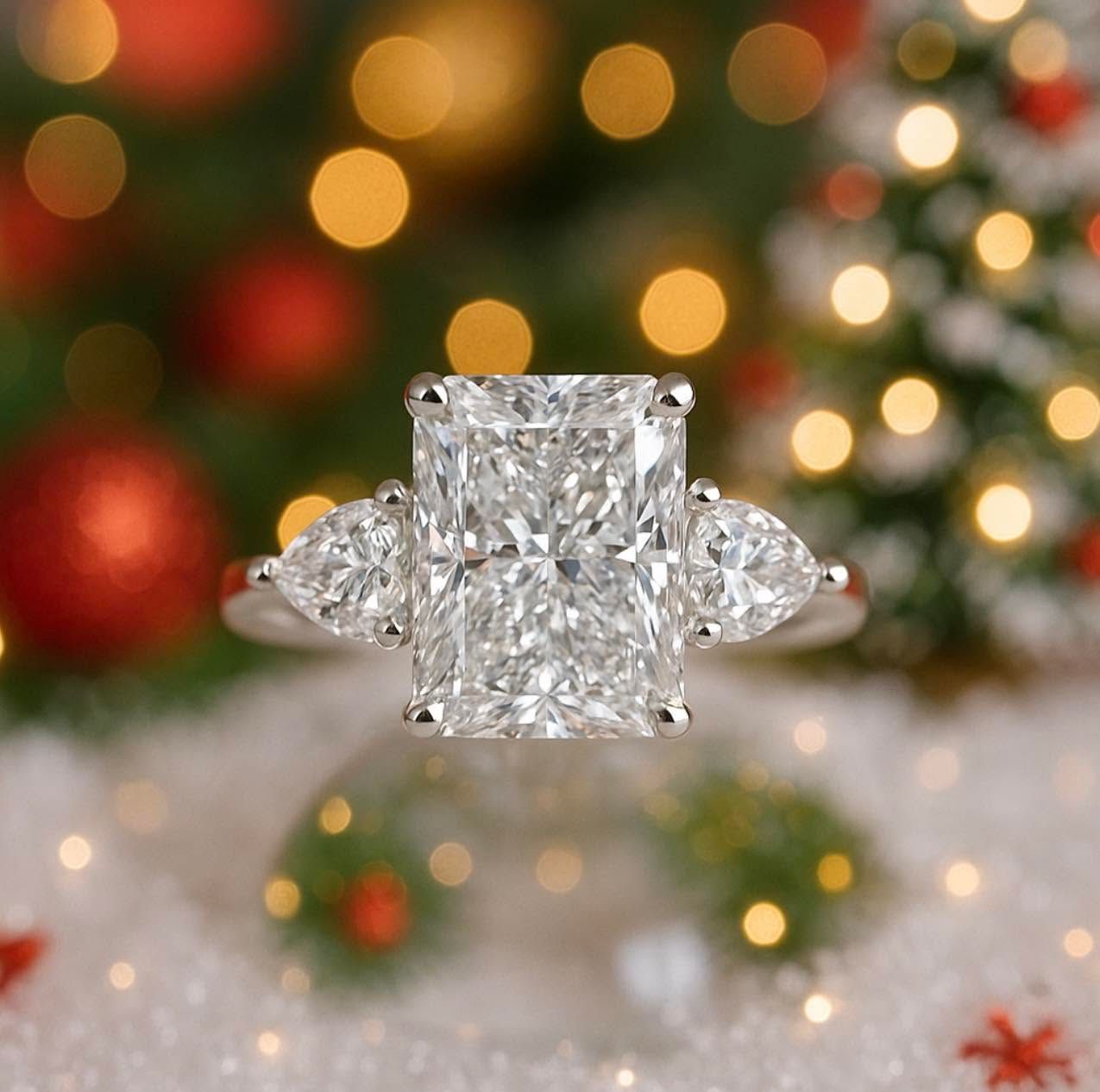 Diamond ring with side stones on a white surface, with festive blurred Christmas lights in the background