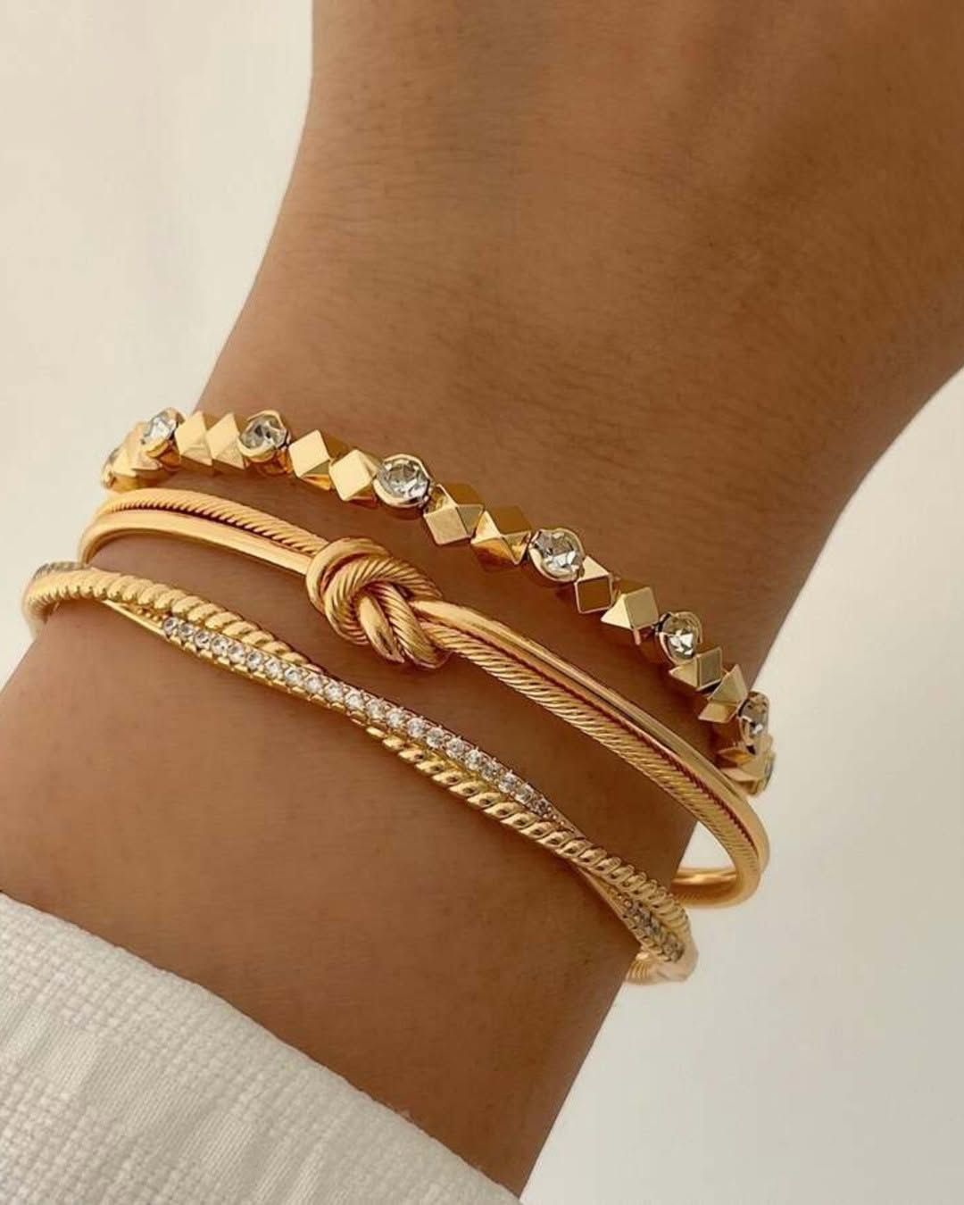 Gold beaded and knot bracelets on a wrist against a neutral background