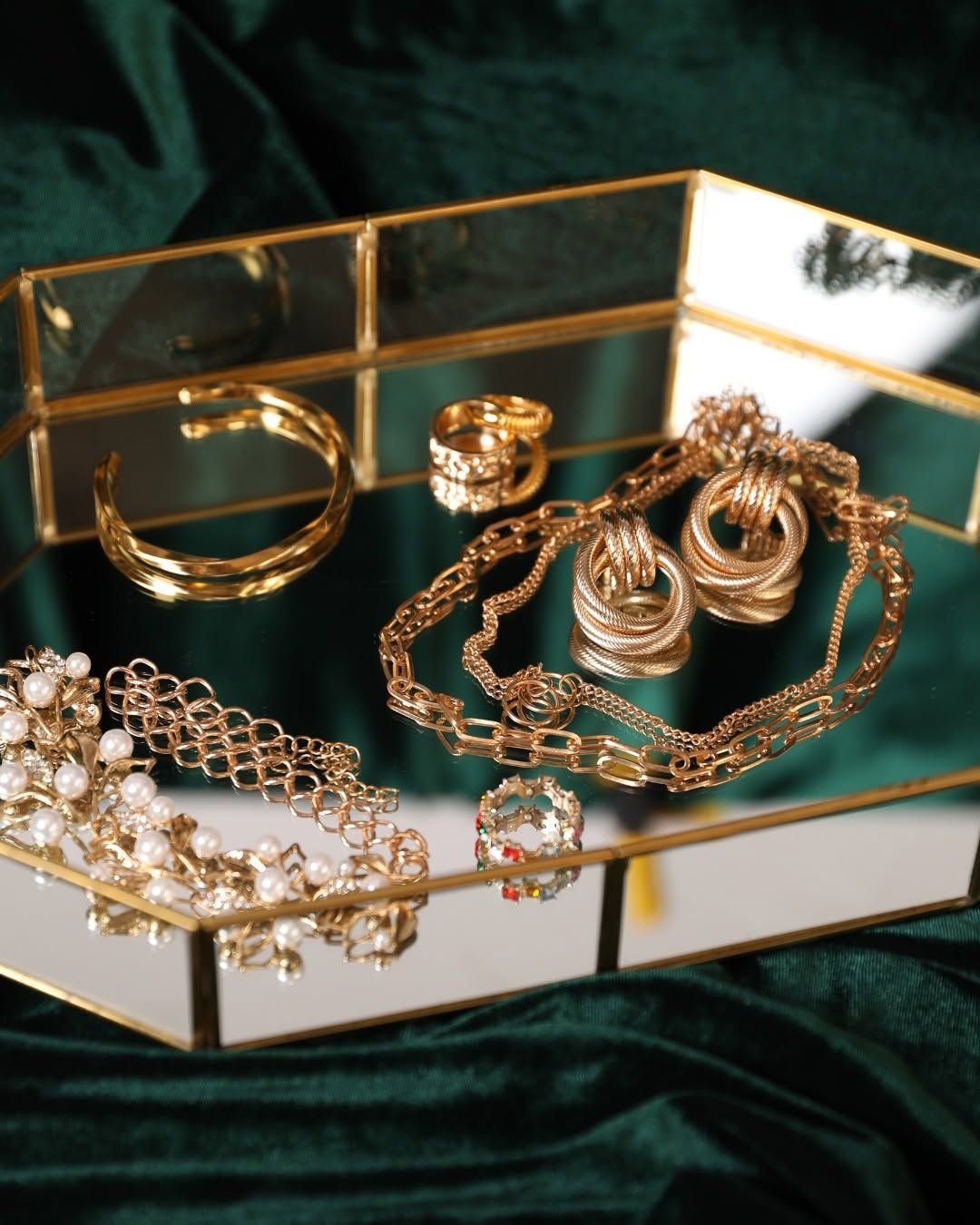 Gold and pearl jewelry arranged in a mirrored tray on dark green velvet.