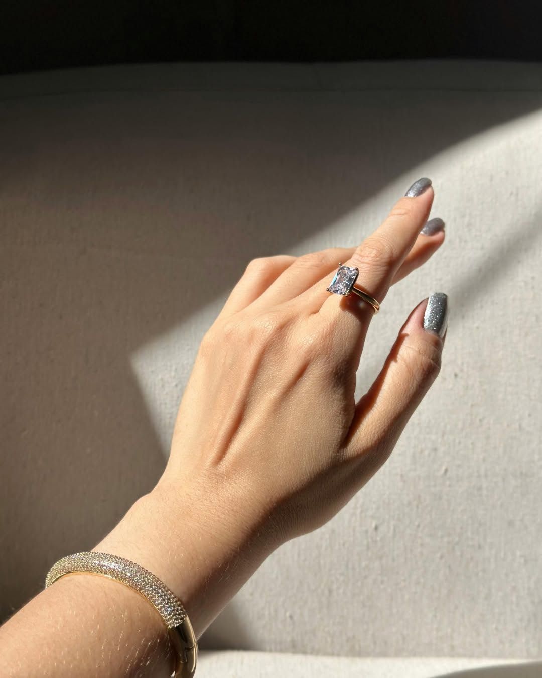 Hand with silver nails and rings resting on a sunlit beige surface.
