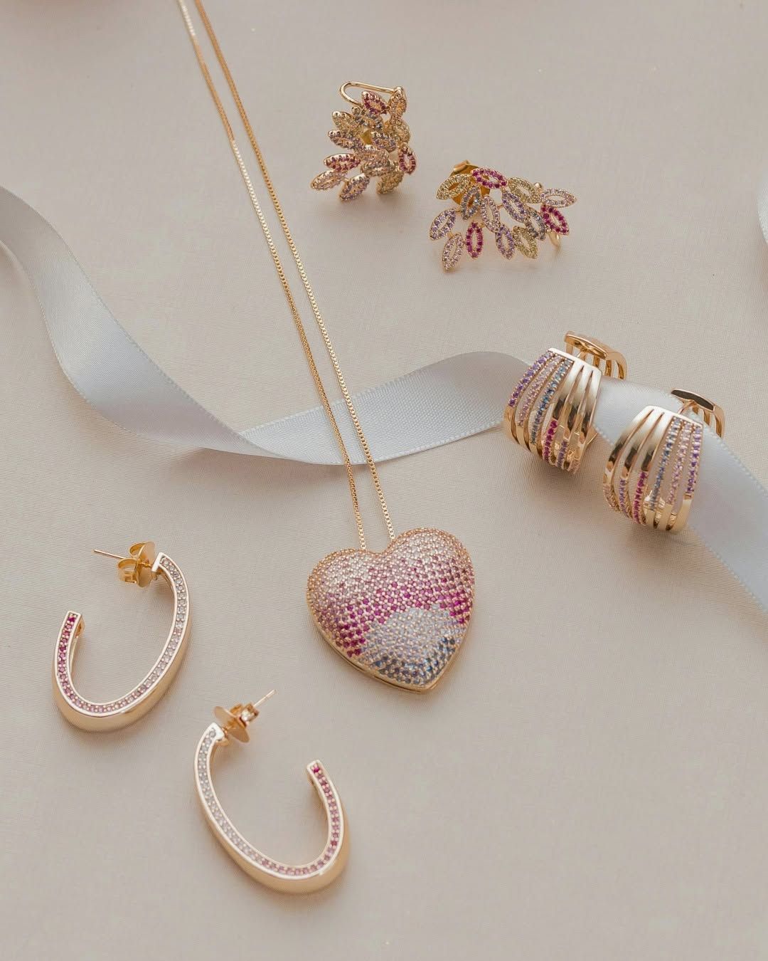 Pink and gold jewelry set with heart pendant, hoops, rings, and earrings on a light surface