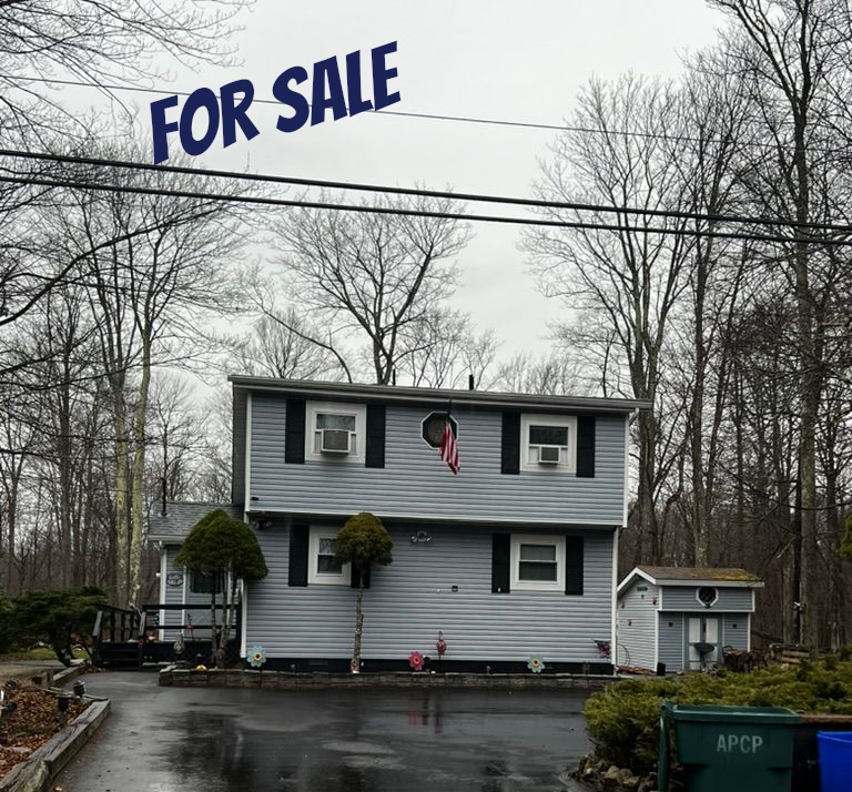 Two-story house with a large “FOR SALE” sign above it on a rainy day