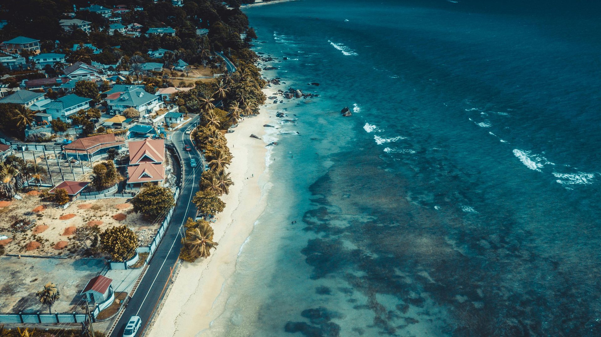 Aerial view of a sandy beach beside turquoise ocean and shoreline buildings