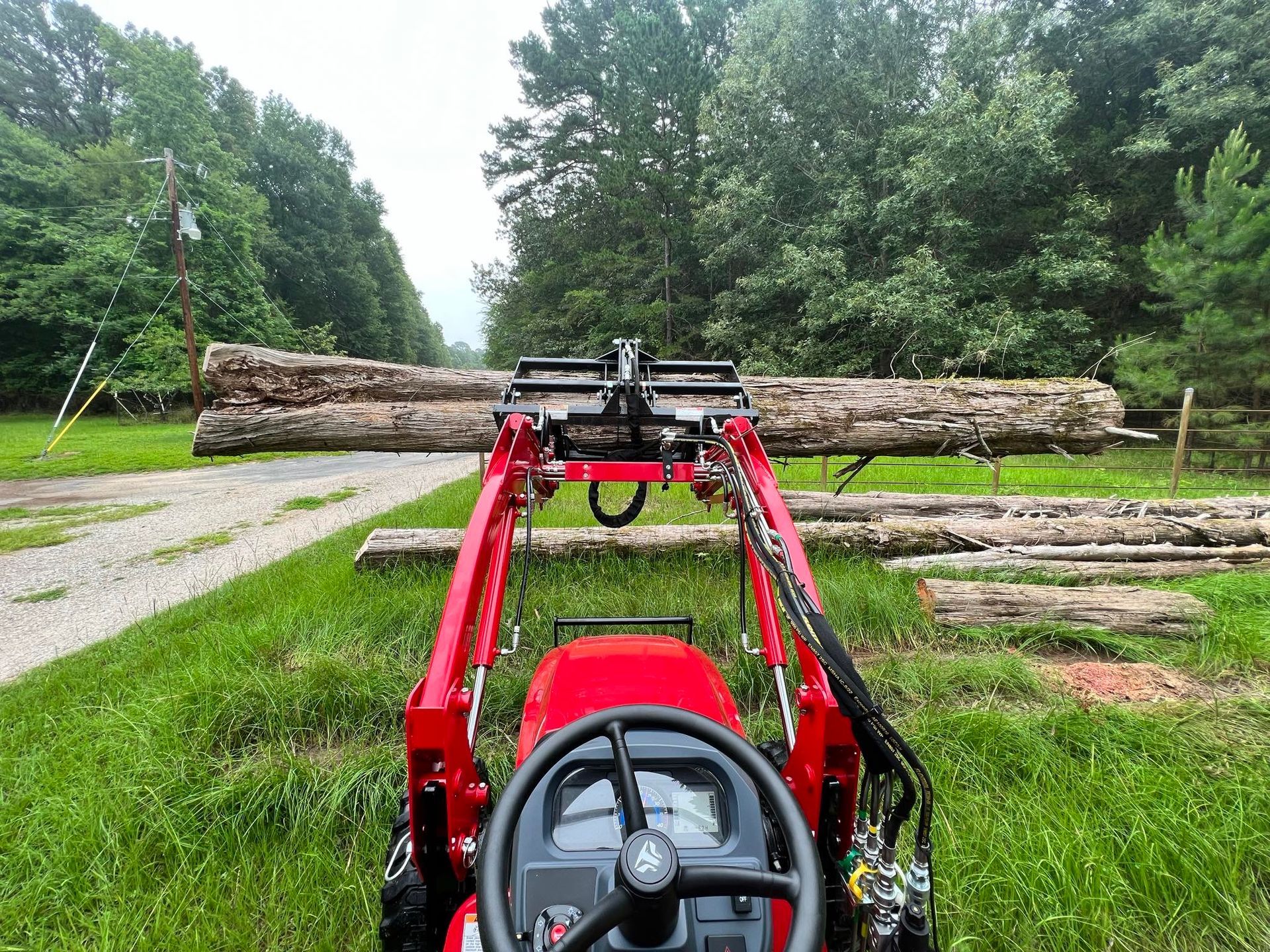 A red tractor is carrying logs down a dirt road.