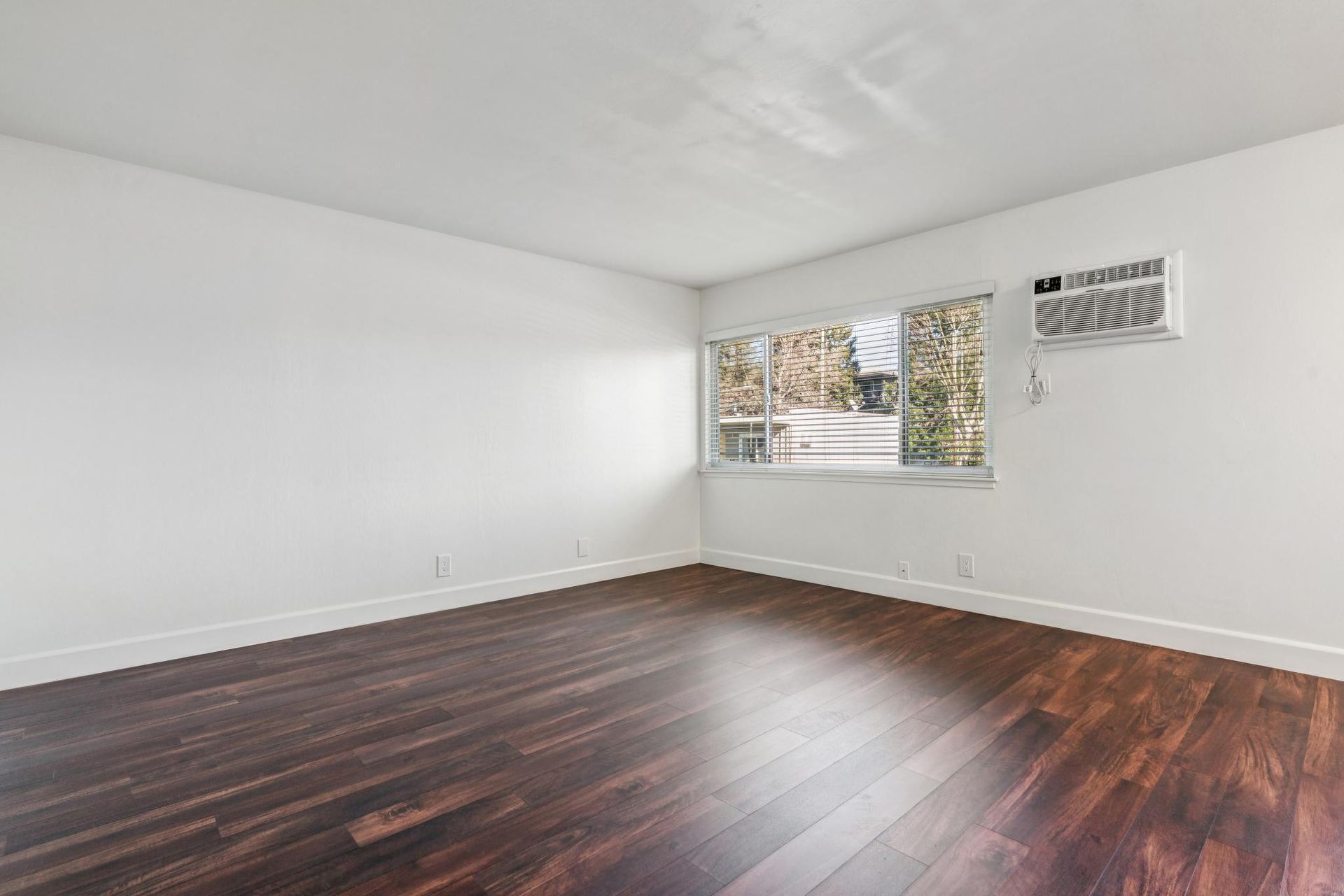 Empty white room with dark hardwood floors and a window air conditioner.