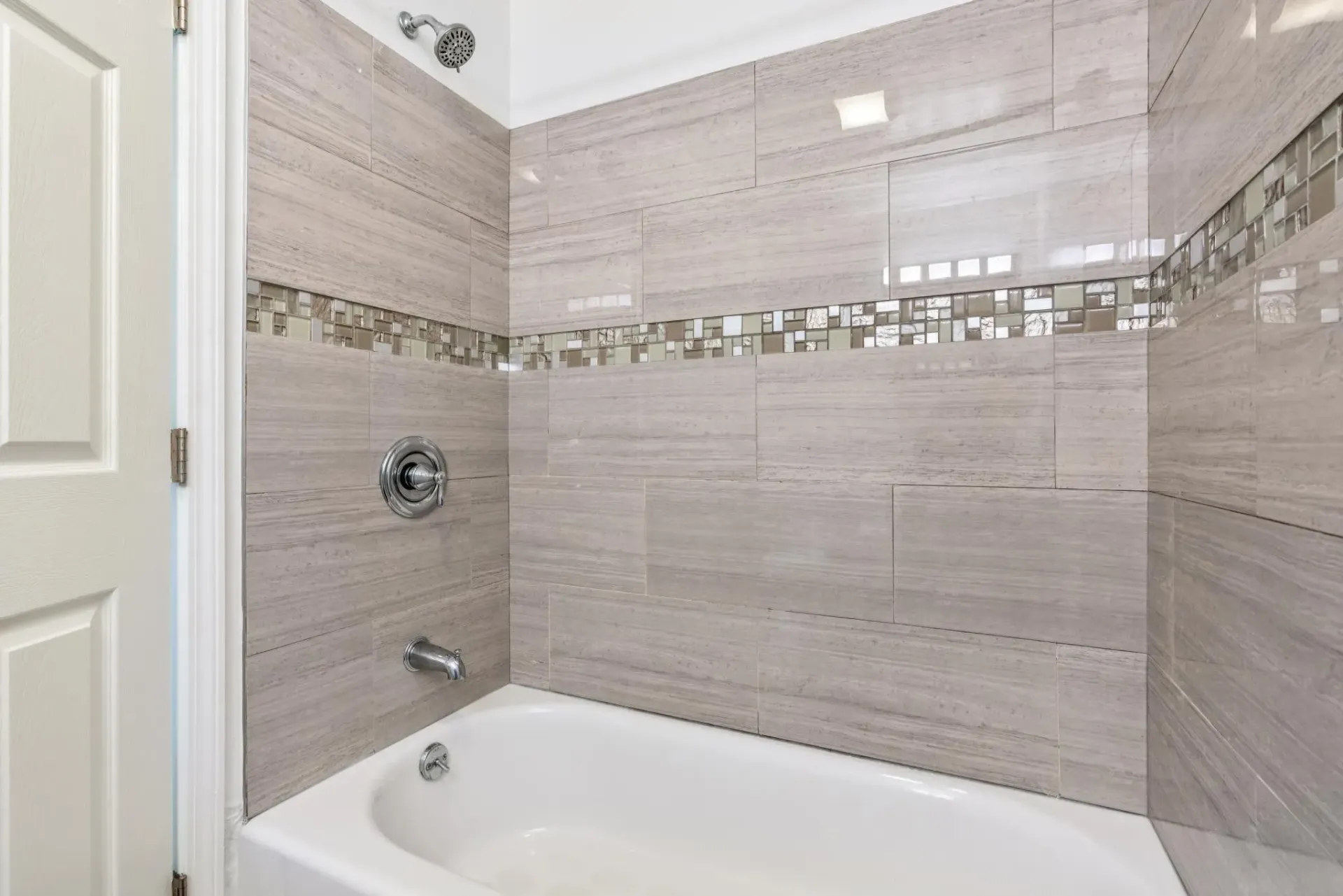 Bathtub with neutral tile surround and a decorative mosaic strip along the wall.