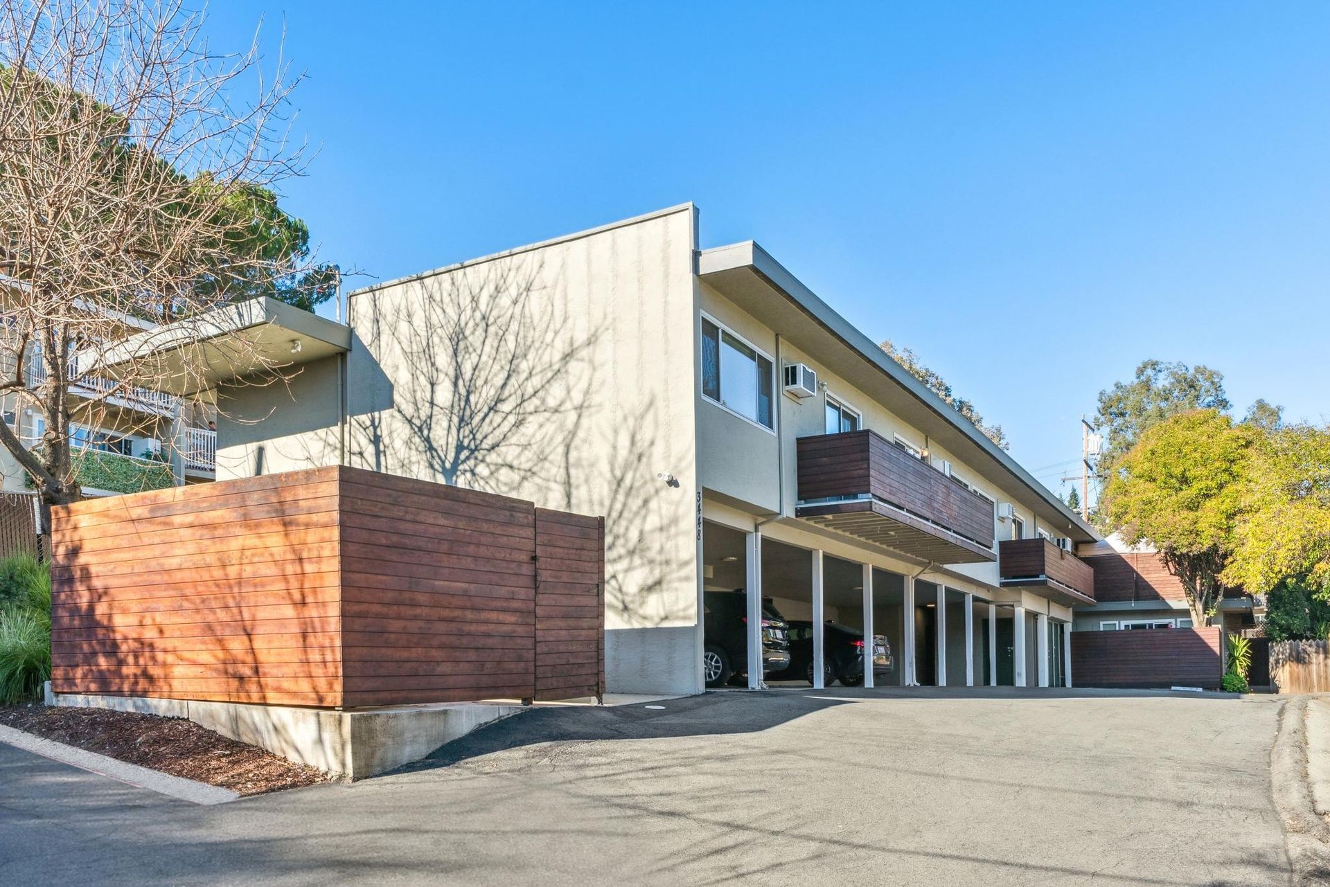 Modern beige building with wood accents and covered parking spaces under a clear blue sky