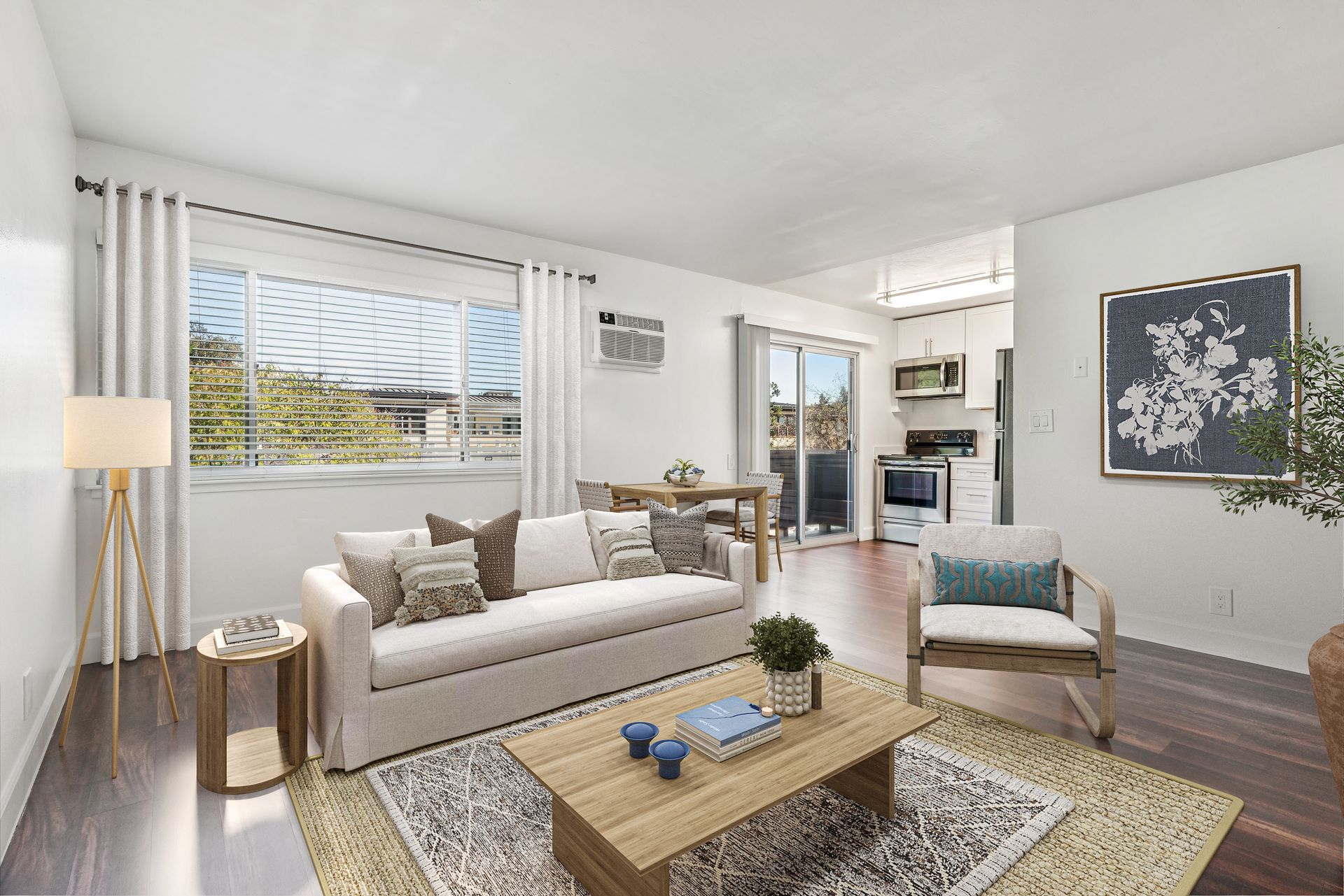 Bright living room with beige sofa, coffee table, patterned rug, and large windows with white blinds