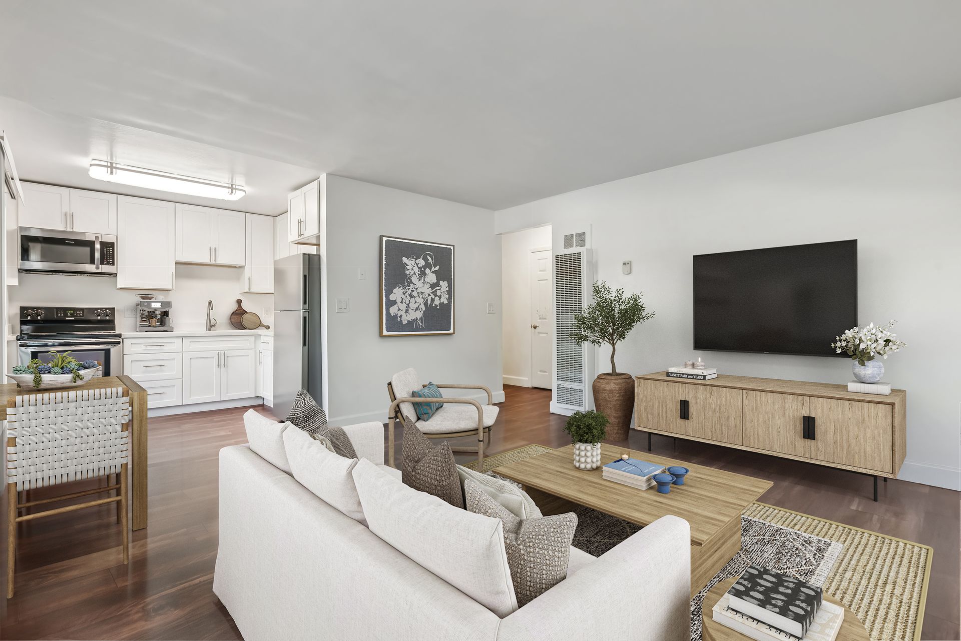 Bright modern living room with white sofa, woven coffee table, TV, and open kitchen in the background