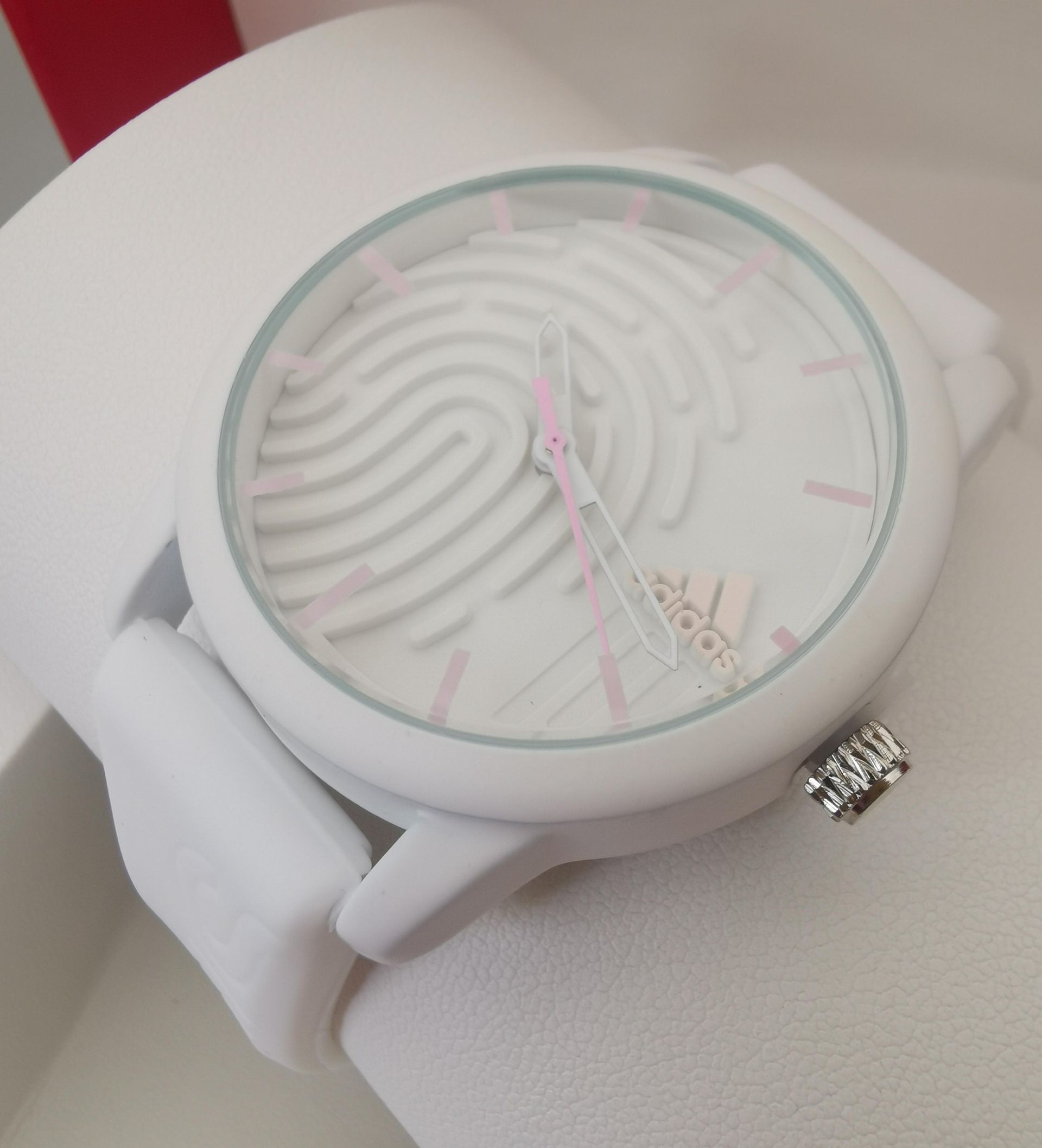 Reloj Adidas de color blanco con diseño de huella dactilar en la esfera y agujas rosas.