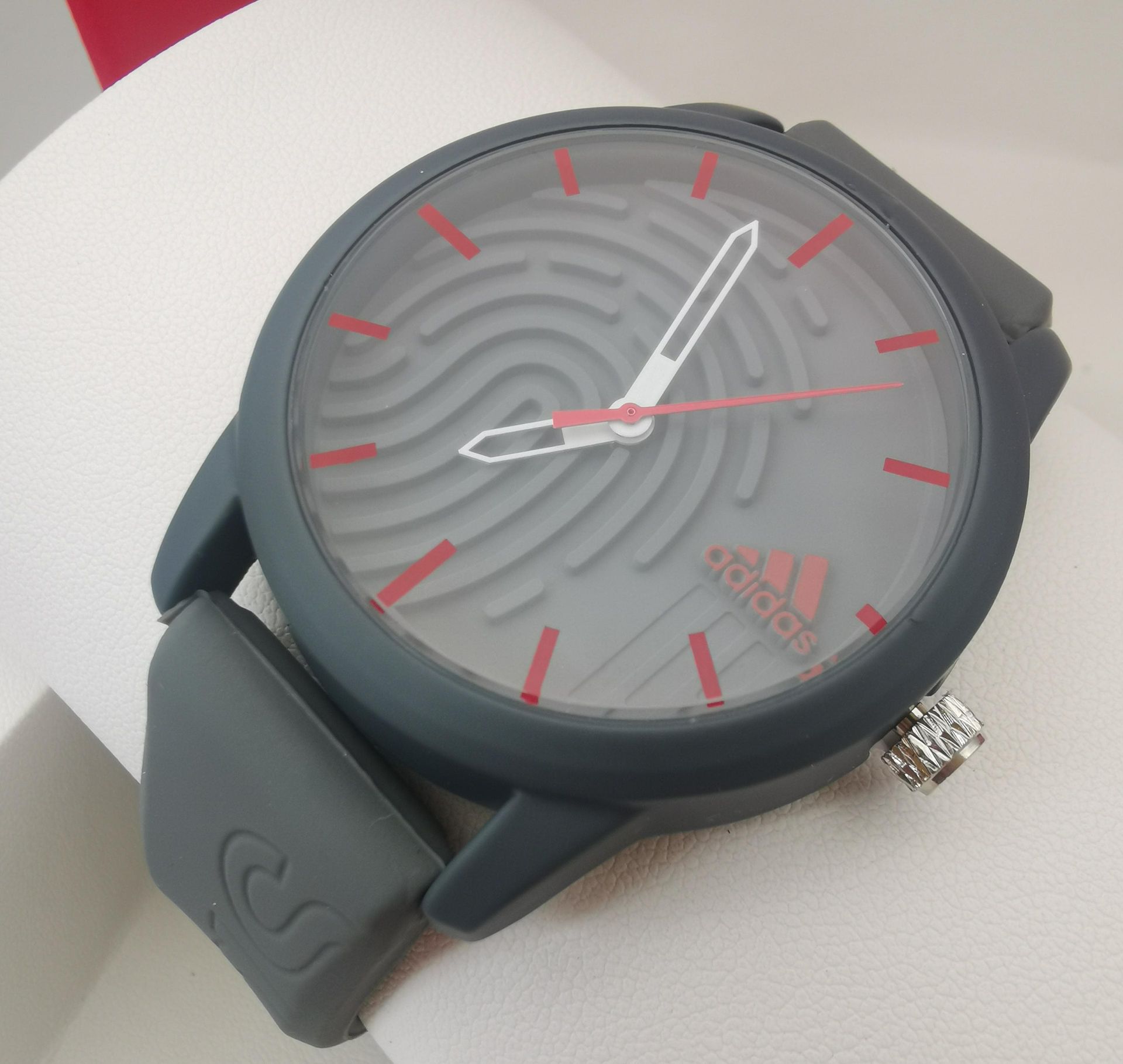 Reloj Adidas de color blanco con diseño de huella dactilar en la esfera y agujas rosas.