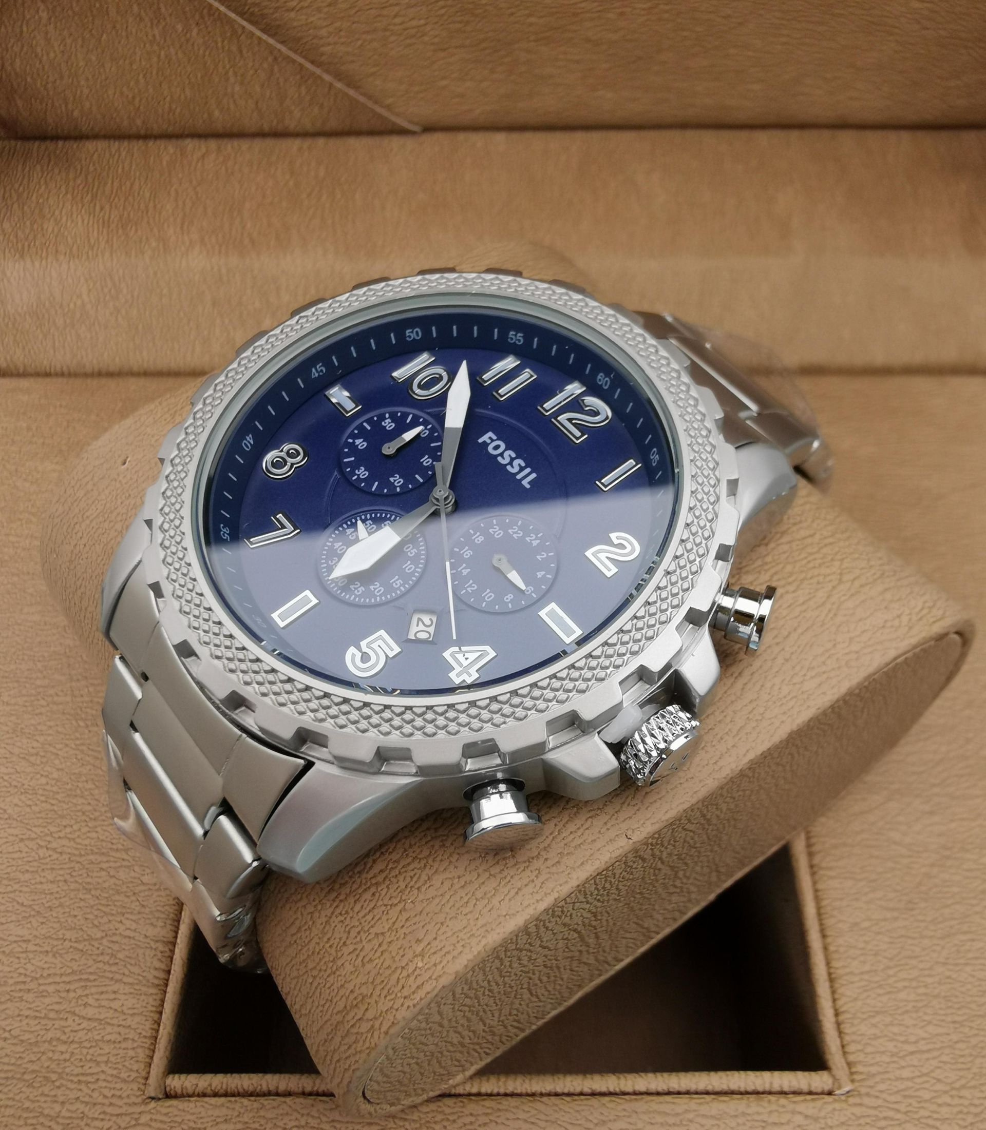 Reloj Fossil plateado con esfera azul y bisel adornado con diamantes, apoyado sobre un soporte de reloj marrón.