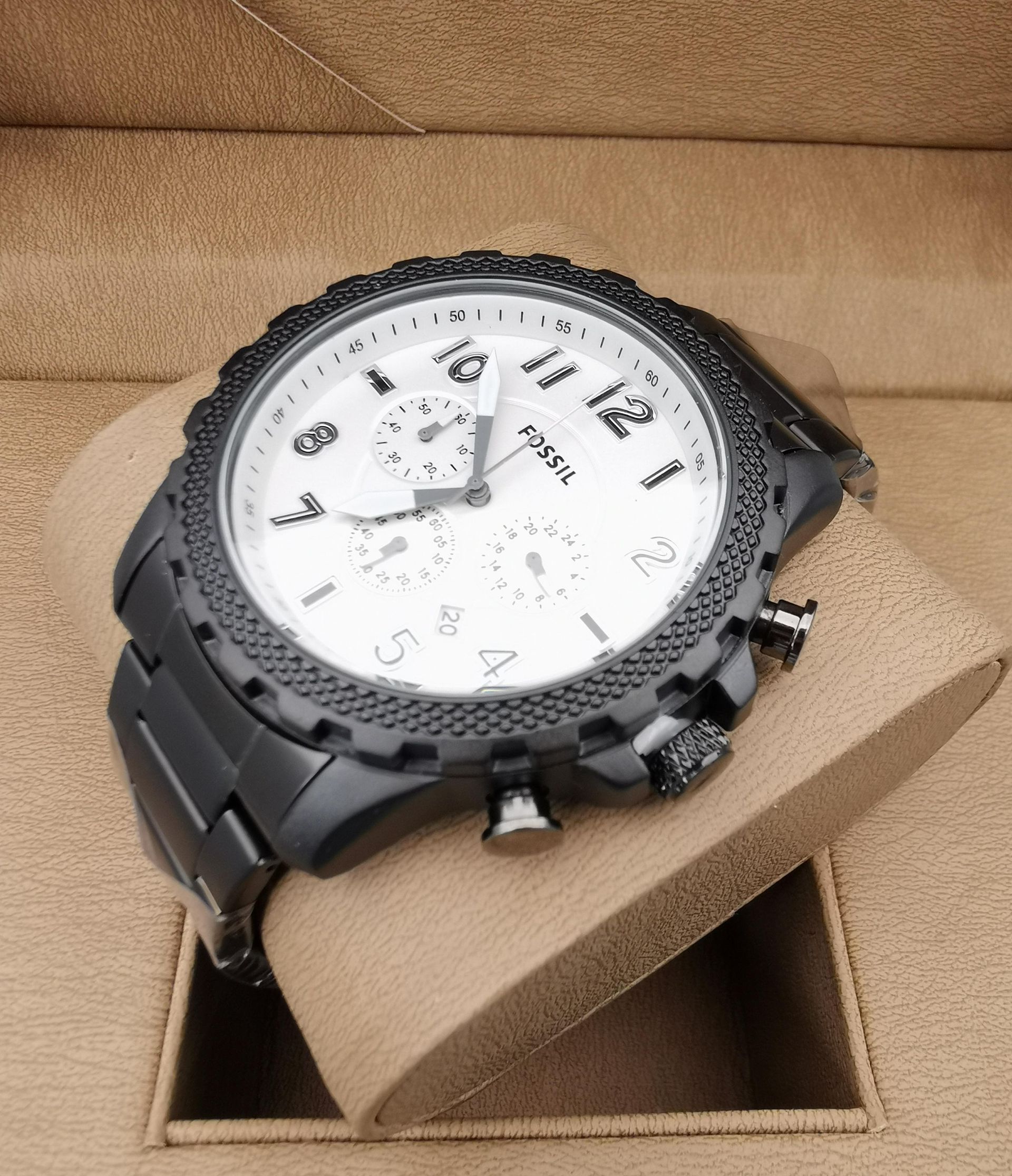 Reloj Fossil plateado con esfera azul y bisel adornado con diamantes, apoyado sobre un soporte de reloj marrón.