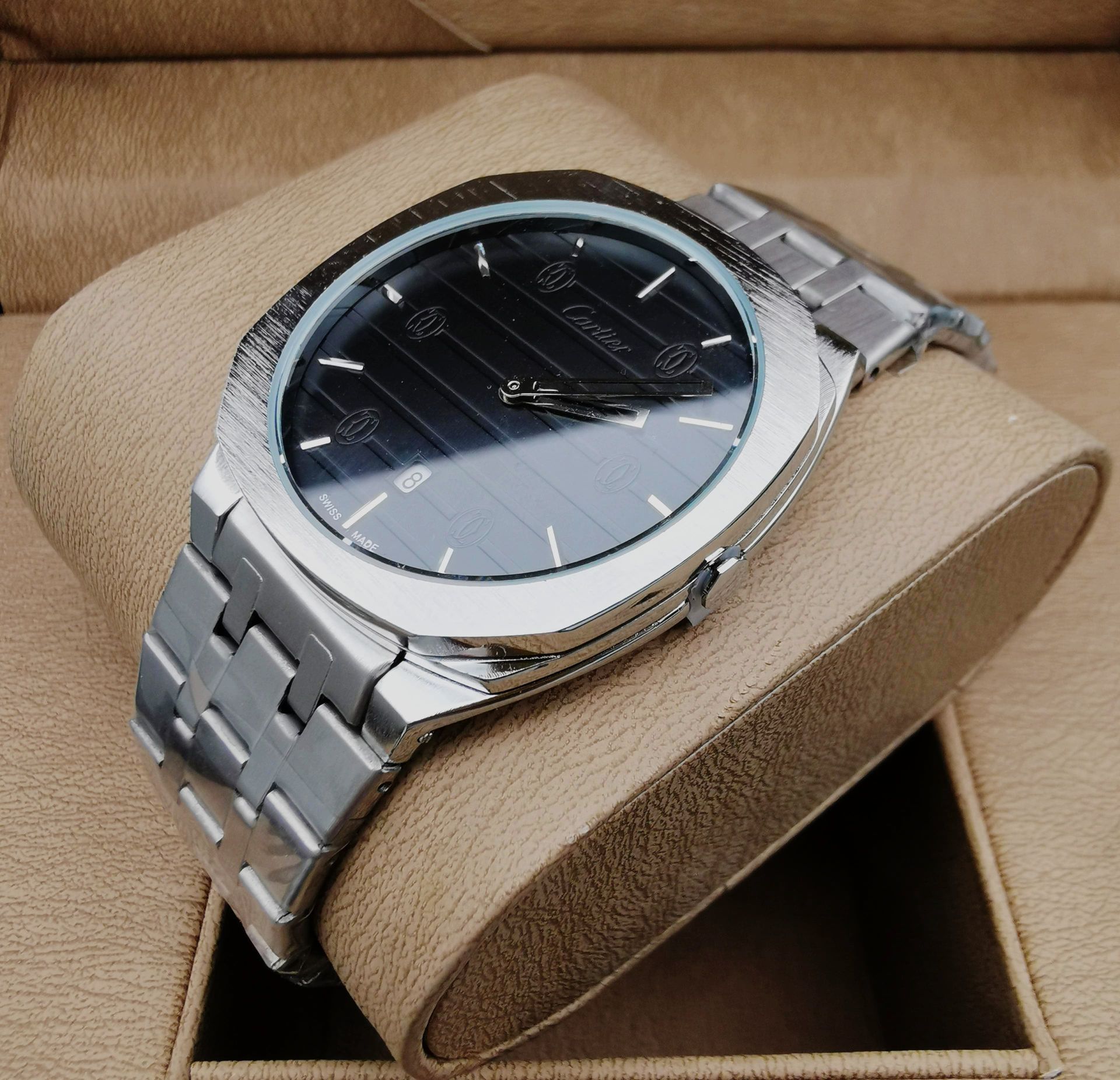 Reloj de pulsera plateado con esfera negra sobre pantalla color tostado.