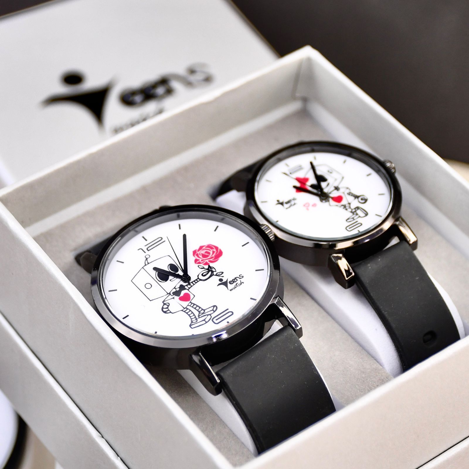 Par de relojes en una caja de regalo, cada uno con cara blanca, correa azul y diseño de manecillas de dibujos animados.