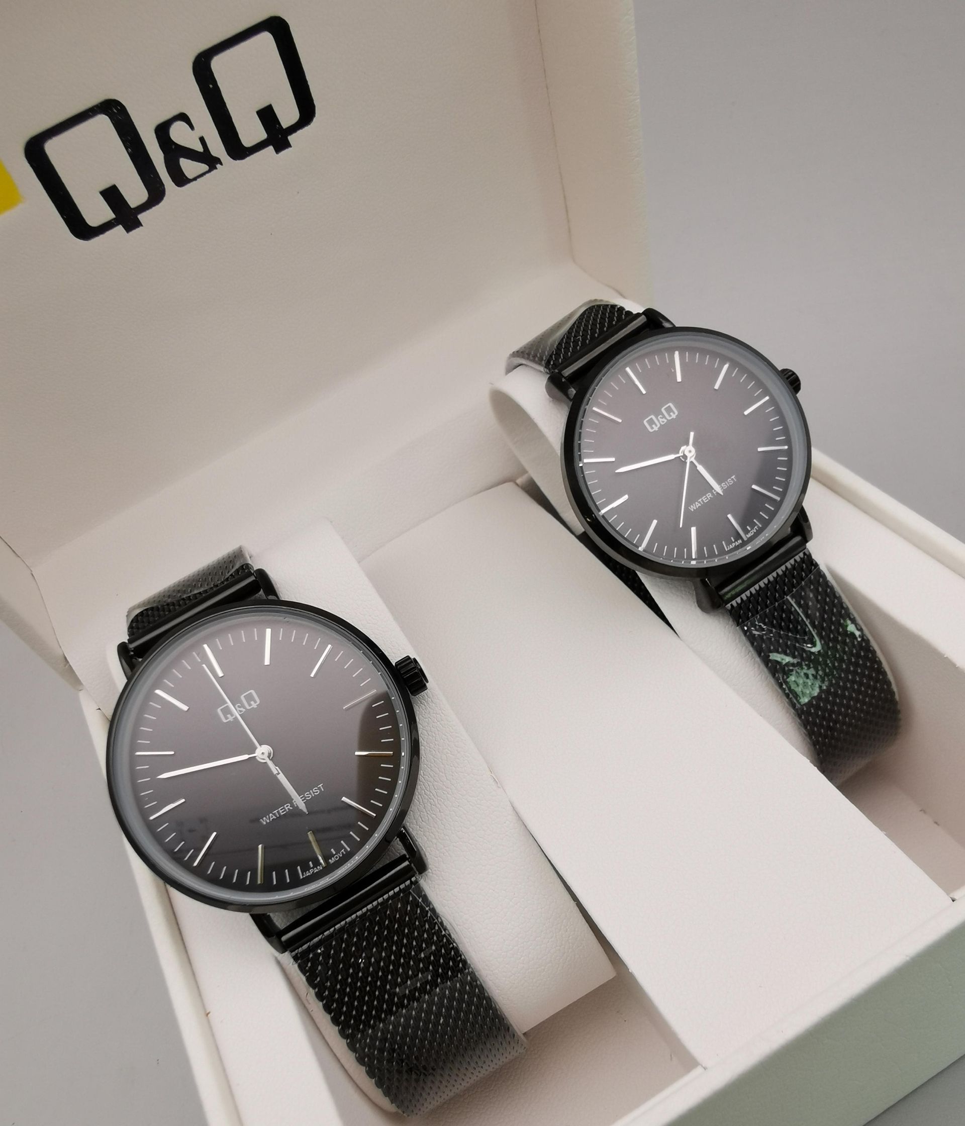 Dos relojes dorados Q&Q con correas de malla en una caja de regalo blanca, con esferas de color claro.