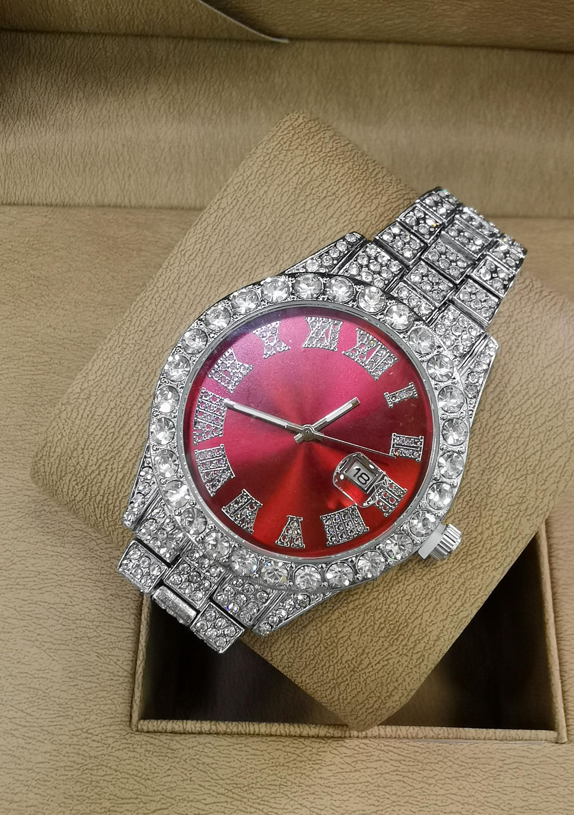 Reloj de pulsera con incrustaciones de diamantes y esfera roja, que reposa sobre un cojín beige en un joyero.