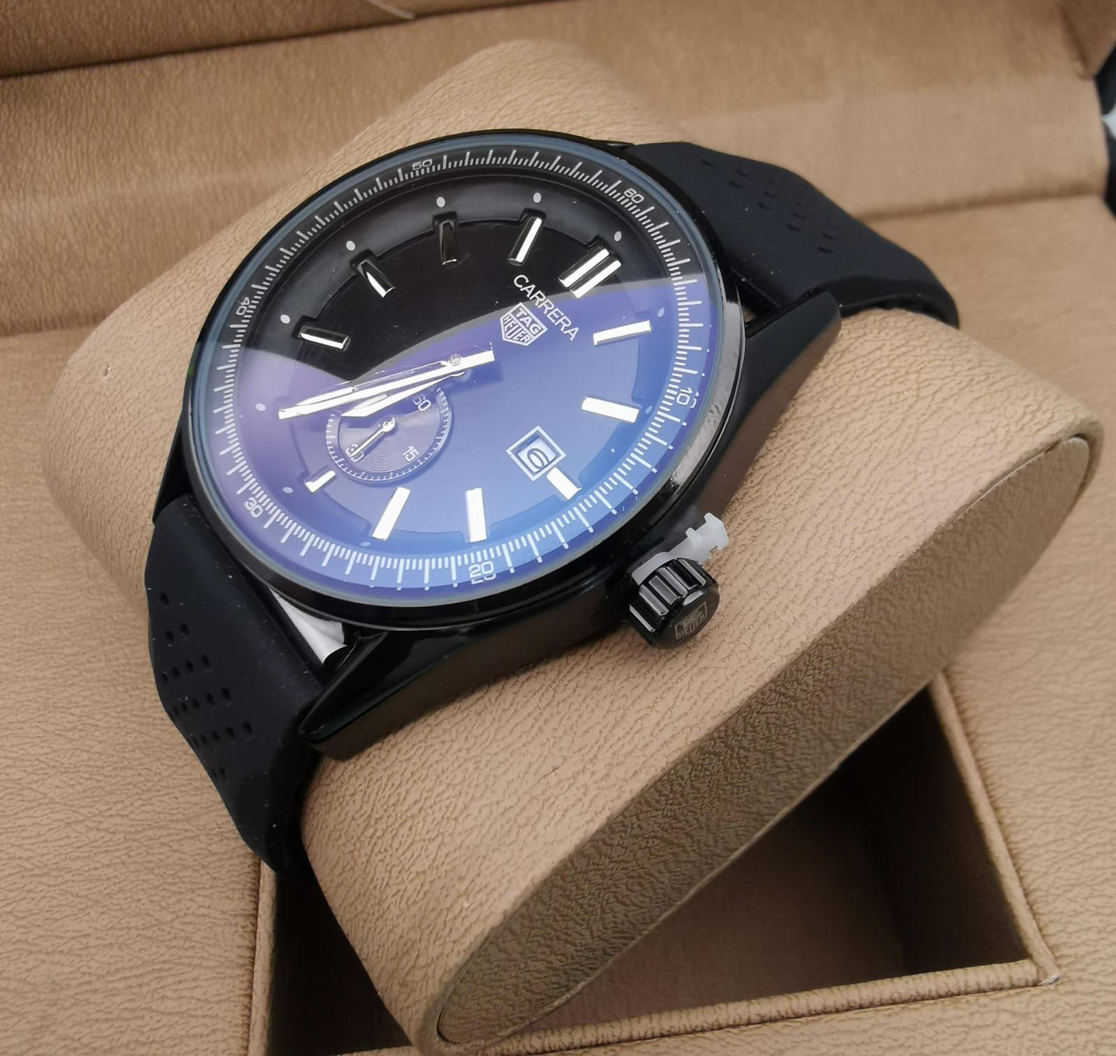 Reloj de pulsera negro con correa de caucho negra sobre una base de reloj de color beige.