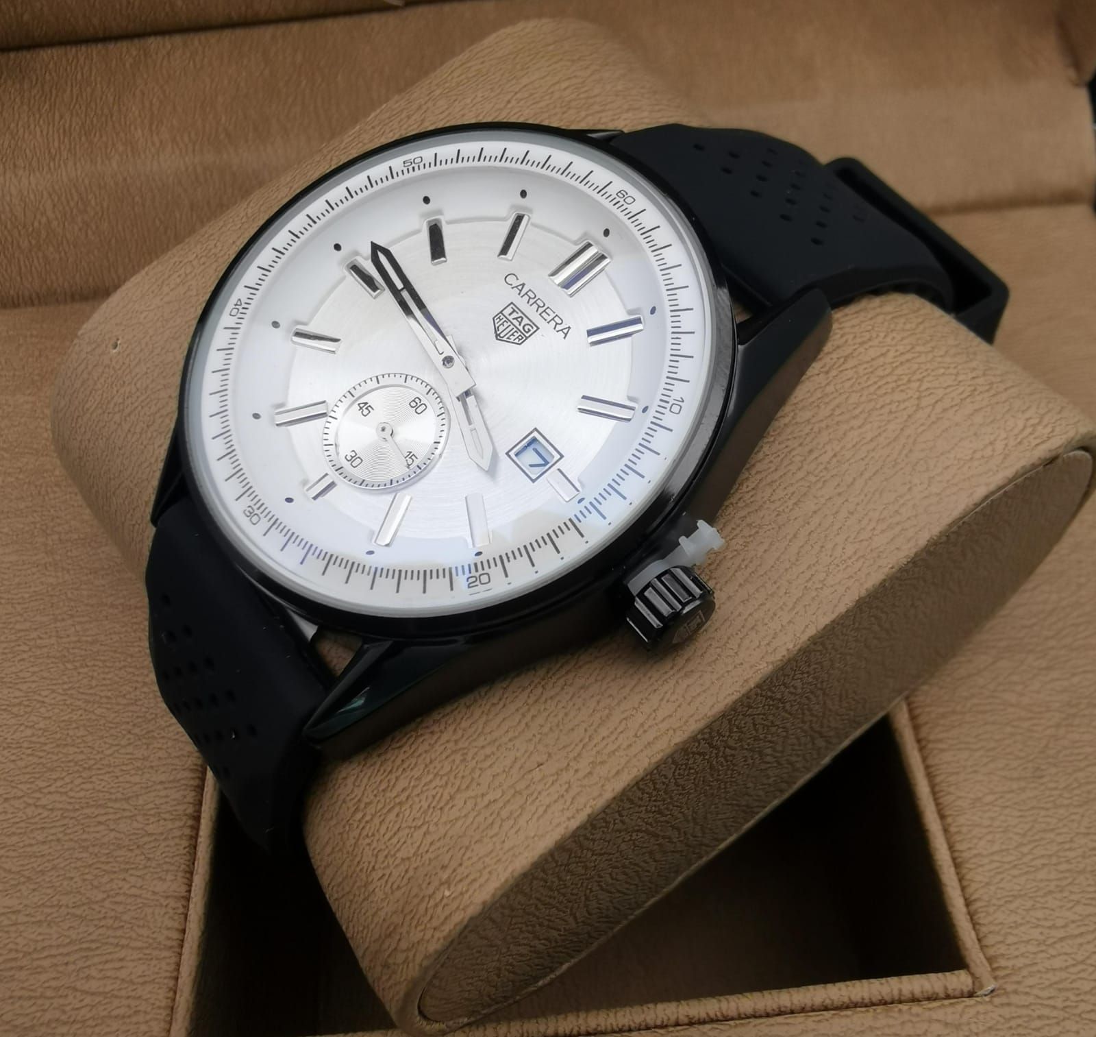Reloj de pulsera negro con correa de caucho negra sobre una base de reloj de color beige.