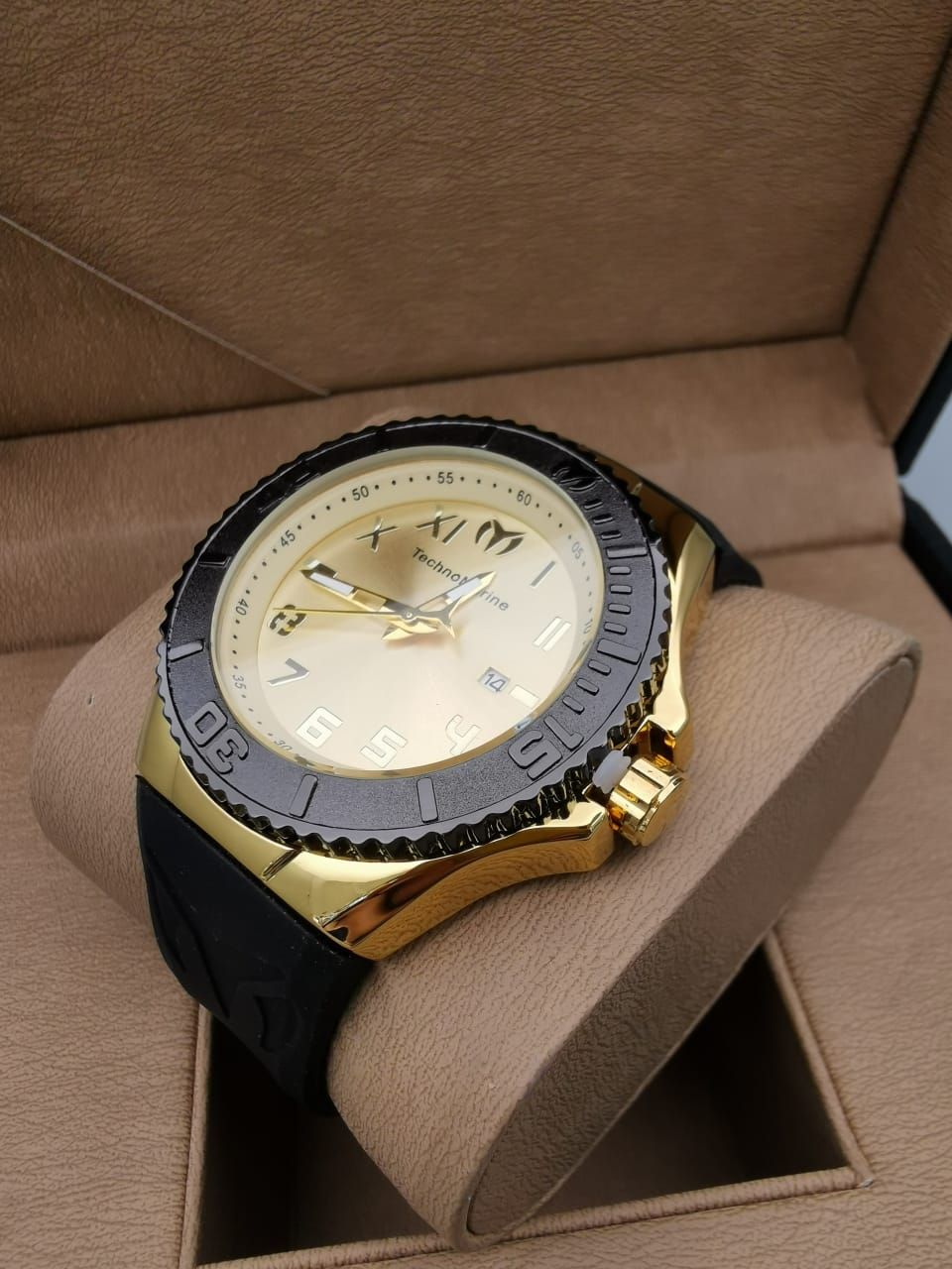 Reloj de pulsera dorado y negro sobre un cojín beige dentro de una caja marrón.