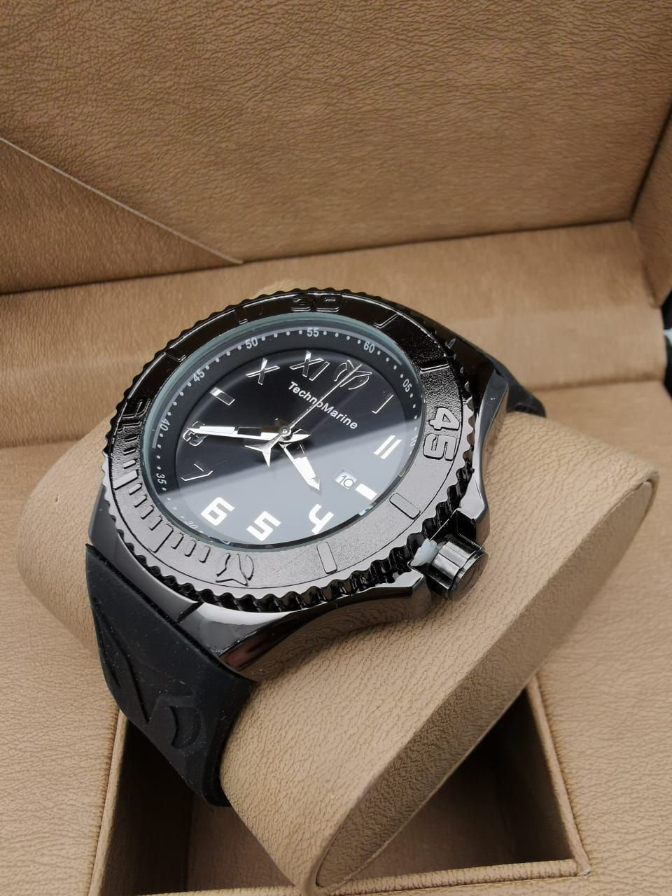 Reloj de pulsera dorado y negro sobre un cojín beige dentro de una caja marrón.