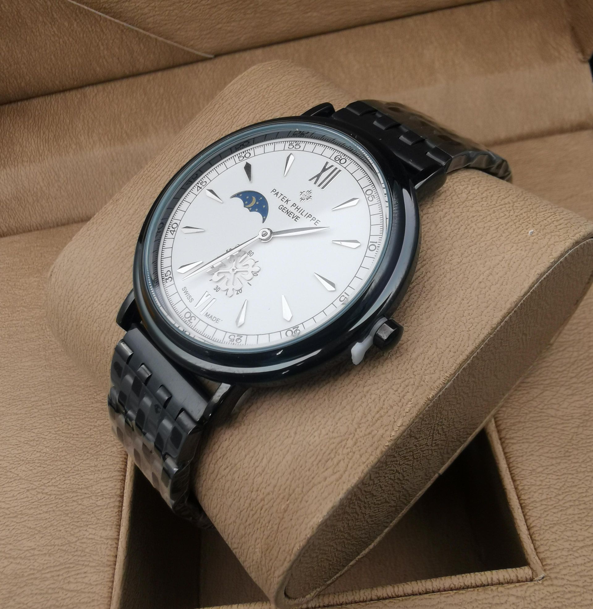 Reloj de pulsera plateado con funciones de fase lunar y calendario sobre una almohada de reloj de color bronce.