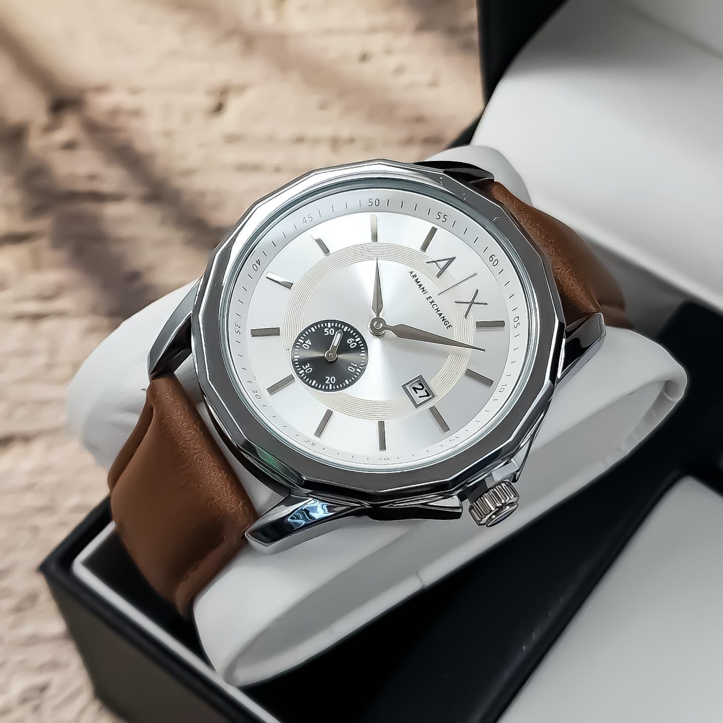 Reloj de pulsera plateado con correa de piel marrón en caja.