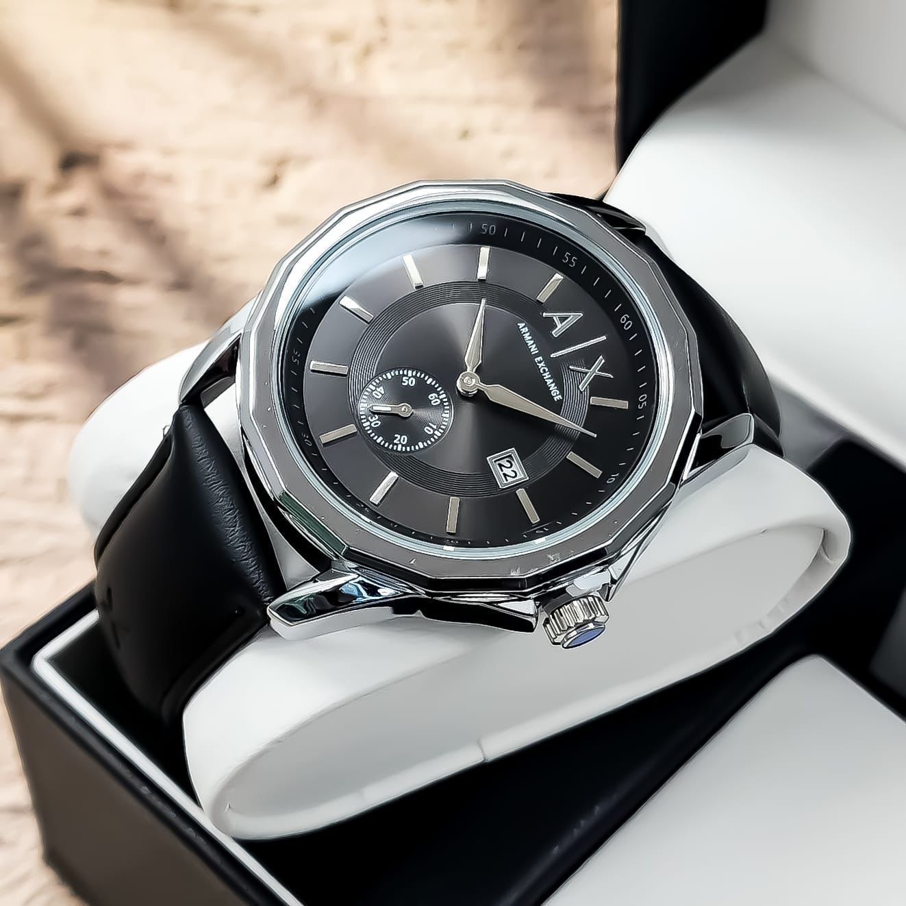 Reloj de pulsera plateado con correa de piel marrón en caja.