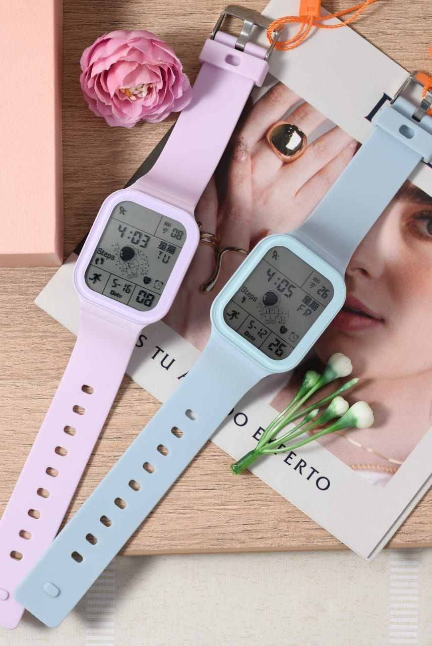 Dos relojes digitales de color pastel con caras rectangulares sobre una superficie de madera con una flor y etiquetas.