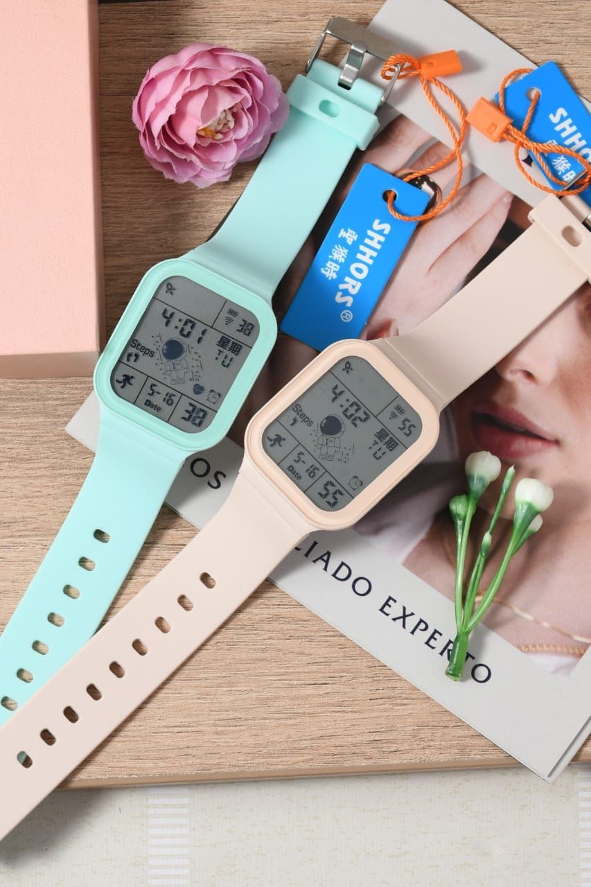 Dos relojes digitales de color pastel con caras rectangulares sobre una superficie de madera con una flor y etiquetas.