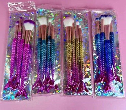 Cuatro juegos de pinceles de maquillaje con forma de cola de sirena en un empaque transparente, cada uno con mangos