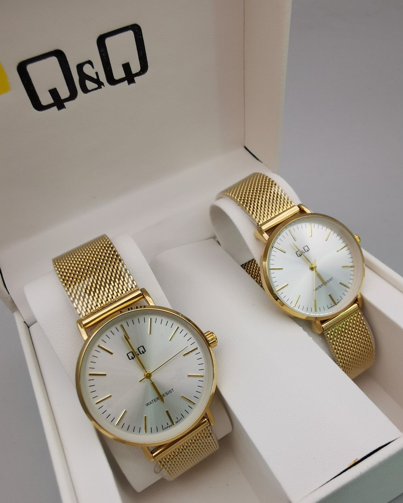 Dos relojes dorados Q&Q con correas de malla en una caja de regalo blanca, con esferas de color claro.