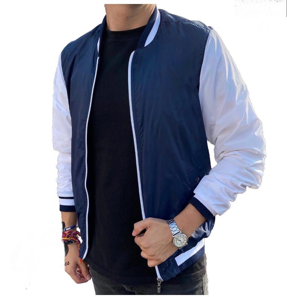 Hombre vestido con chaqueta bomber azul marino y blanca y camisa negra.