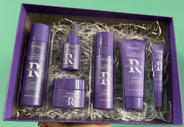 Set de cuidado de la piel de color morado en caja de regalo, que incluye botellas, suero y cremas, sobre un fondo verde.