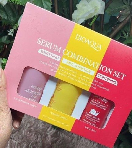 Una mano sosteniendo un set combinado de sueros BIOAQUA en un empaque rosa, amarillo y rojo.