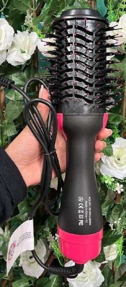 Mano sosteniendo un cepillo secador de pelo negro y rosa con un cordón, rodeado de flores blancas.