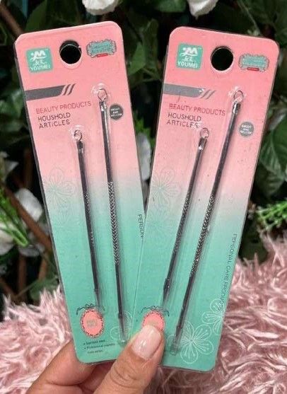 Dos paquetes de herramientas para eliminar puntos negros en una mano. Envase rosa y verde, con diseño de flores blancas.